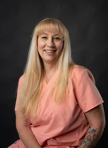 The image shows a woman with blonde hair wearing an orange scrub top, posing for a portrait with a neutral background.