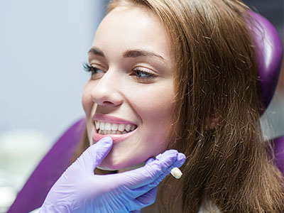 A young woman with a bright smile sits in a dental chair, receiving professional attention from a dentist.