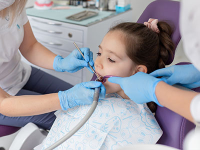 A young girl receiving dental treatment with a dentist using a drill on her teeth.