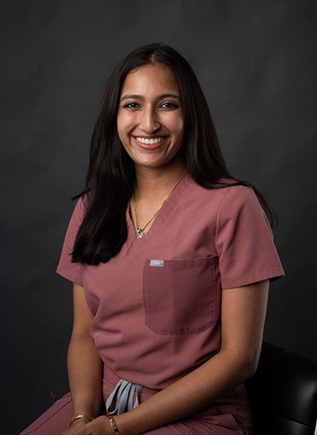 The image shows a woman wearing a scrubs uniform, smiling at the camera, with a neutral background.